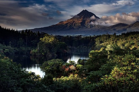 Mount Taranaki rises majestically above Lake Mangamahoe surrounded by lush greenery, New Zealand,