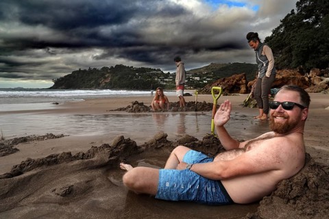 Man relaxing in sand pit on cloudy Hot Water Beach, Coromandel Peninsula, Waikato, New Zealand