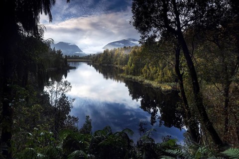 Lake Matheson offers a tranquil reflection of the surrounding mountains and forests in soft morning