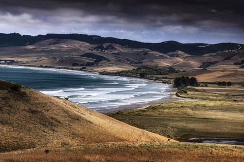 Waves break on Katiki Point beach surrounded by rolling hills, Katiki Point, New Zealand