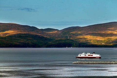 Hurtigruten ship off the wooded hills of Hammerfest on calm water, Hammerfest, Finnmark, Norway