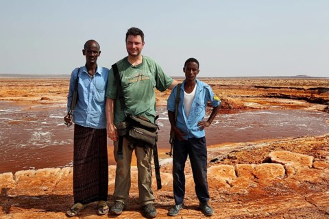 Three men stand at a hot spring in the desert of Dallol, Dallol, Ethiopia