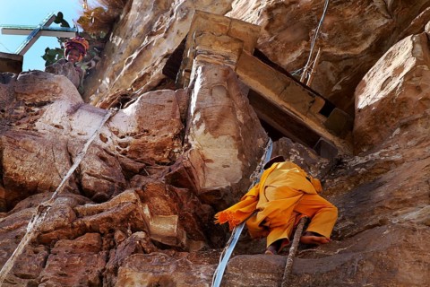 A monk climbs a rope to the entrance on rocky ground, Debre Damo, Tigray, Ethiopia