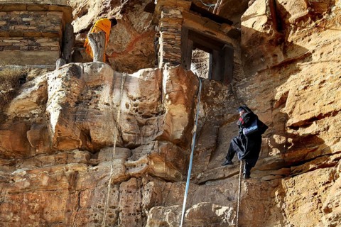 A monk climbs a rope to a monastery entrance on rocky terrain, Debre Damo, Tigray, Ethiopia