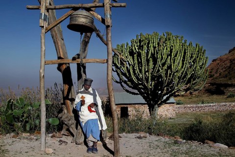 Priest next to a bell near the rock church Debre Mariam Krokor, zero