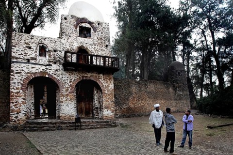 Stone gate building with arched windows and people surrounded by trees
