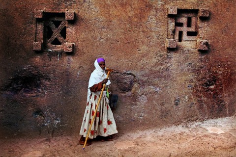 Woman in colorful clothes leaning against a decorated church wall, Lalibela, Amhara, Ethiopia