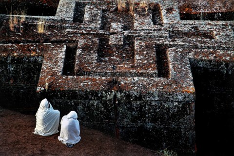 Two veiled pilgrims pray in front of the impressive Bete Gyorgis, Lalibela, Amhara, Ethiopia