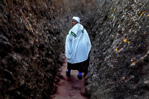 A person wearing traditional clothing walks through a narrow rocky passage near Bete Gyorgis,