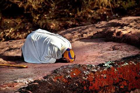 Kneeling person praying on rock, expressing deep faith near Bete Gyorgis, Lalibela, Amhara,
