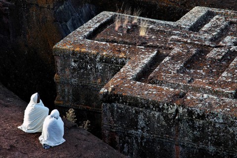 Historic rock church of Bete Gyorgis in Lalibela with two believers in traditional clothing,