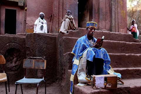 A priest reads in front of the rock church of Bete Gyorgis in Lalibela, Lalibela, Amhara, Ethiopia