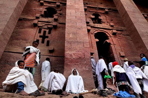 Pilgrims wearing white cloaks gather solemnly in front of the Bete Medhane Alem rock church at