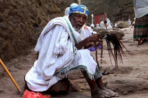 A praying monk in traditional clothing on a stone path, Lalibela, Amhara, Ethiopia