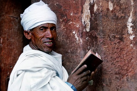 A man in traditional dress reads with a smile on a stone wall, Lalibela, Amhara, Ethiopia