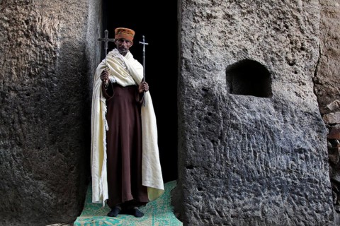 Priest with crosses standing in stone niche, Lalibela, Lasta Mountains, Ethiopia