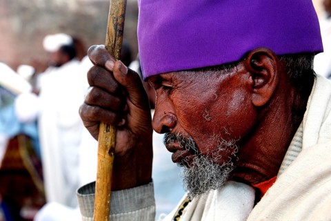 An elderly man wearing purple head covering prays at Bete Maryam church during Easter, Lalibela,