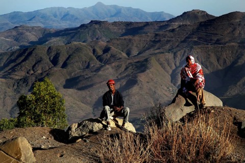 Two people sit in front of the impressive mountain scenery of the Lasta Mountains, Lalibela,