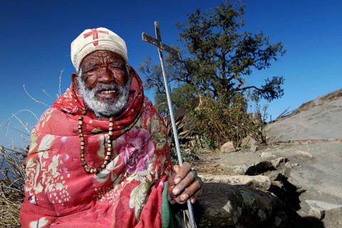 Priest with colorful blanket and cane in mountainous landscape, Lalibela, Lasta Mountains, Ethiopia