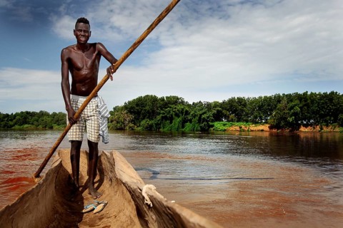 Man navigates in a dugout along the Omo River, surrounded by thick vegetation, Omorate, Ethiopia