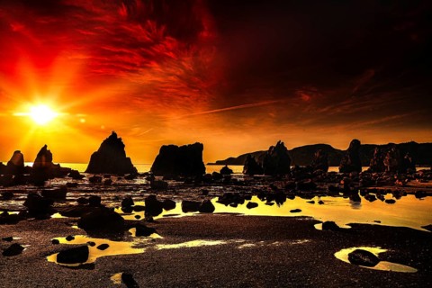 Fiery red sunrise over coastal rock formations with intense reflections, Kushimoto, Japan