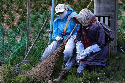 Two fabric figures sitting in the garden holding brooms