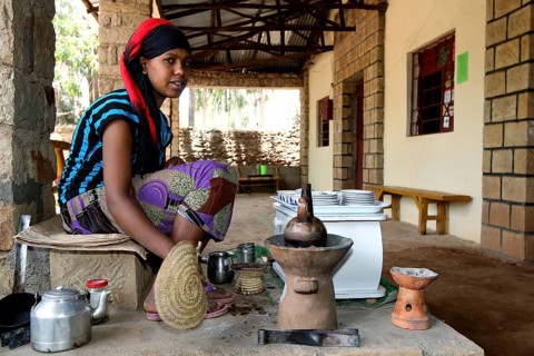 Woman preparing traditional coffee ceremony in a covered area, with ritual objects, Yeha, zero,