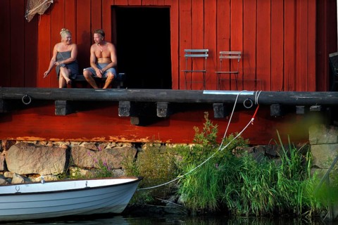 Couple sitting at a red warehouse on the shore with a boat at the water, Porvoo, Uusimaa, Finland