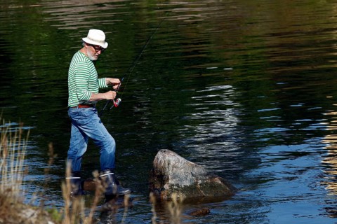 Angler with hat standing in water at a calm lake, Suomenlinna, Helsinki, Finland