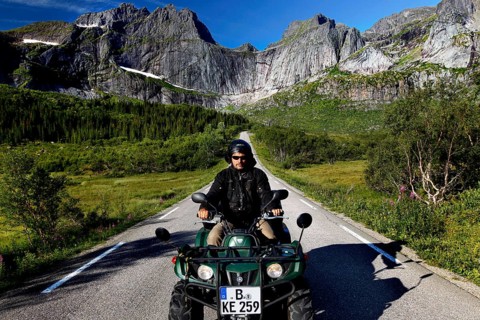 Man riding ATV on road in the mountainous landscape of Flakstadøy, Nusfjord, Flakstadøy, Norway