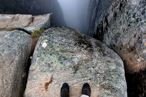 Two feet stand on a rock looking into the depths of Kjeragbolten, Lysefjord, Rogaland, Norway