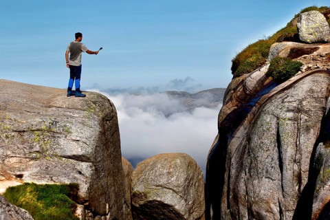 Tourist taking a selfie on cliffs near Kjeragbolten with clouds in the background, Lysefjord,
