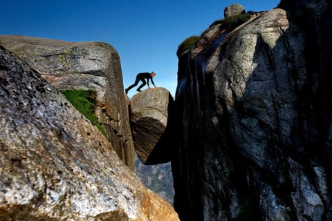 Tourist balancing on Kjeragbolten between imposing cliffs under blue sky, Lysefjord, Rogaland,