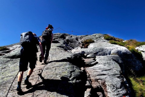 Hikers climbing Kjerag with safety chain and blue sky, Lysefjord, Rogaland, Norway