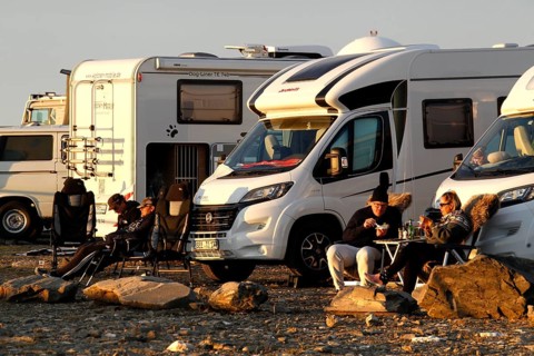 Campers relax next to motorhomes in a parking lot on the North Cape in the evening sun, North Cape,