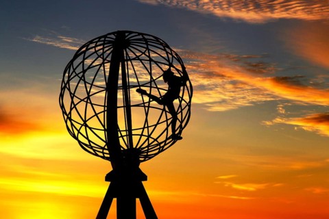 Silhouette of a climber on the North Cape globe in front of a colorful sunset, North Cape,