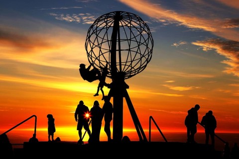 Silhouettes of people on the North Cape globe in front of a glowing sunset, North Cape, Magerøya,