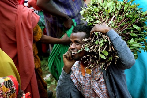 Smiling man carrying khat bundles on his shoulder and talking on the phone at a market, Awaday,