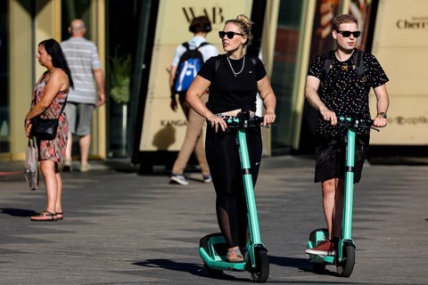 Two people ride scooters on a road in Tallinn when the sun is shining, Tallinn, South Alinn,