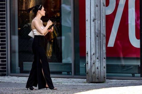 Woman walks by a shop while holding a cellphone and strolling through the neighborhood, Tallinn,