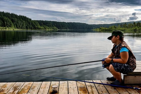 Young fisherman on a jetty on peaceful Ilgis Lake, surrounded by forest in Iginalina, Ignalina,