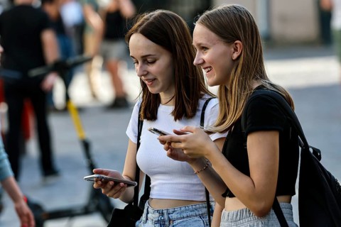 Two young woman laugh together while using their cell phones on the street, Tallinn, Harju, Estonia