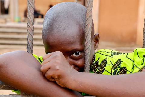 A child looks through metal mesh, a soft smile on his face, Bouké, region, Côte d'Ivoire