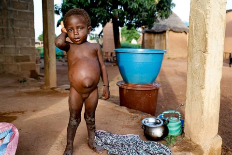 Child standing in front of simple dwellings in a rural village, Nionfouin, zero, Côte d'Ivoire