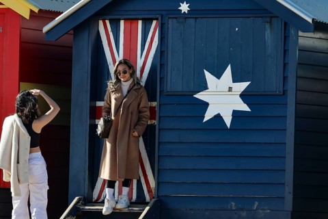 Beach visitors in front of a colorful beach house with flag motif in Brighton Beach, Brighton