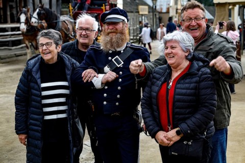 A performer in uniform stands smiling with a group of tourists for photos, Ballarat, Australia