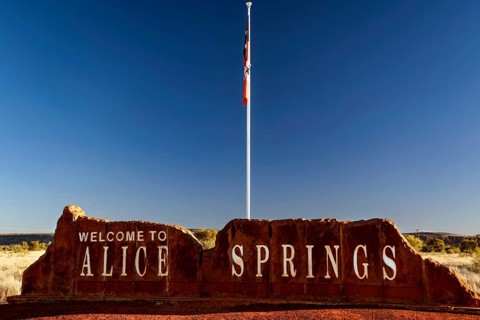 Alice Springs welcome sign with a flag against a clear sky, Alice Springs, Northern Territory,