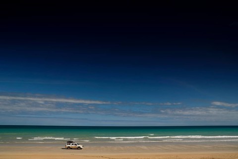 Vehicle on quiet shore of Cable Beach with clear, wide skies, Broome, Western Australia, Australia