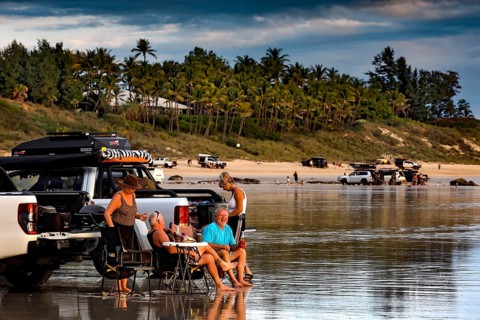 Visitors relax next to cars on Cable Beach car beach, Broome against a palm-covered background,