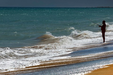 Angler standing on the beach fishing in the waves of Cable Beach, Broome, Broome, Western
